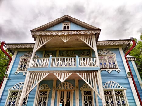 The stunning blue house features detailed wooden designs and a balcony, set against a dramatic cloudy backdrop.