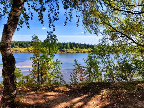 The picturesque river flows gently, surrounded by lush greenery and bathed in sunlight, evoking a peaceful spring atmosphere.