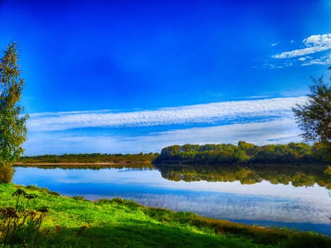 A tranquil lake reflects the clear blue sky, bordered by lush greenery and trees, creating a peaceful natural atmosphere.
