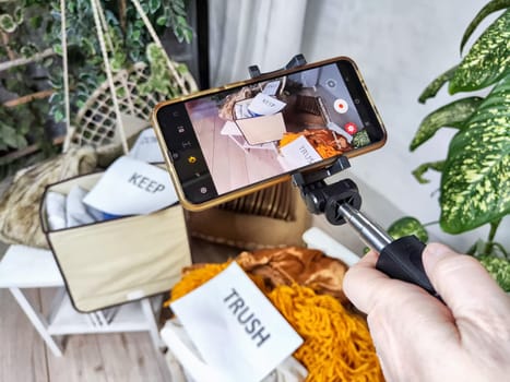 The blogger takes off stacks of clothes and signs with the words save, donate, throw away on cell phone. The concept of clutter, debacle for a blog