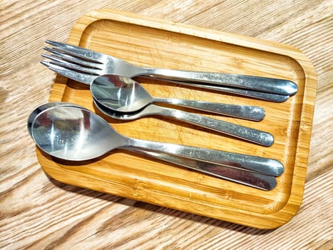 A set of silverware consisting of fork and three spoons is neatly arranged on a wooden tray