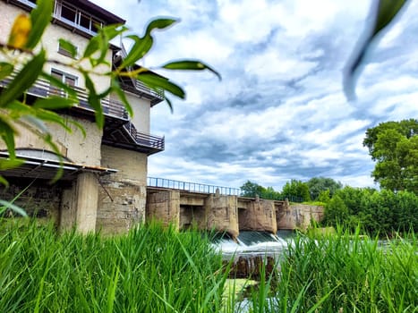 concrete dam with rushing water, surrounded by lush green foliage, on a cloudy summer day