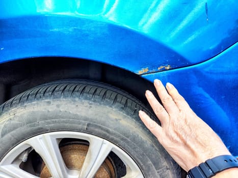 A person is pointing directly at a rusty, weathered place on a car that shows signs of age and decay, highlighting its condition