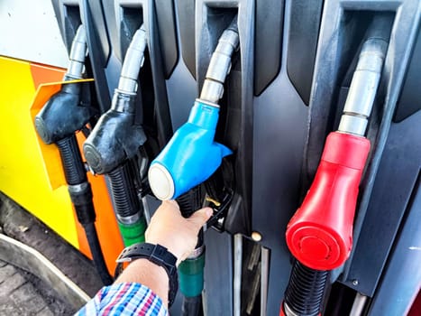 A person is using fuel nozzle to refuel their car at a service station during daylight hours.