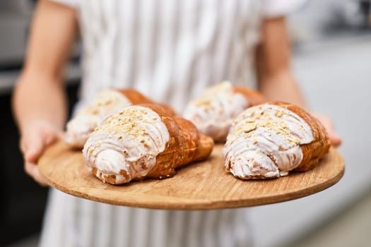 female baker holding wooden tray with freshly baked crispy golden croissants