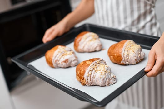 female baker holding metal tray with freshly baked crispy golden croissants