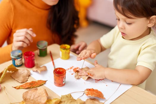 close-up, child and mom hands painting autumn yellow leaves together. happy time together at home