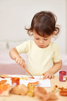 happy little child girl painting autumn leaves. baby girl drawing leaves in yellow and orange paint