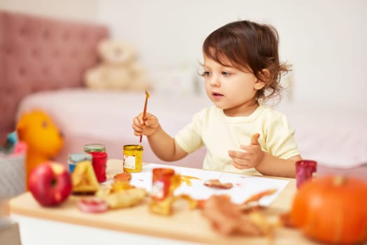 happy little child girl painting autumn leaves. baby girl drawing leaves in yellow and orange paint