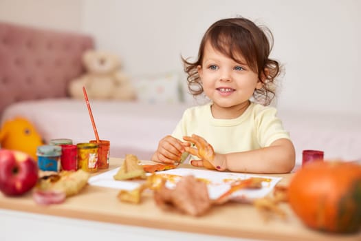 smiling little child girl painting autumn leaves. baby girl drawing leaves in yellow and orange paint