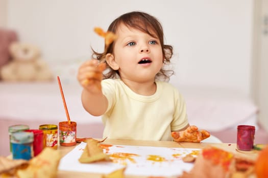 happy little child girl painting autumn leaves. baby girl drawing leaves in yellow and orange paint