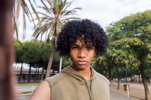 selfie photo looking at camera of a serious african american teenager with curly hair, concept of youth lifestyle and technology of communication