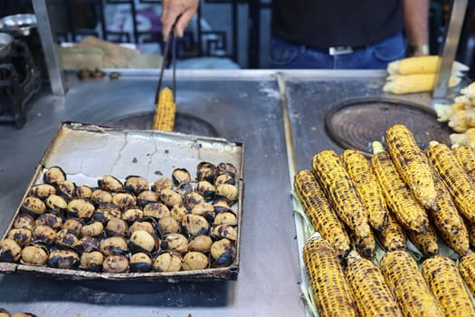 selling fried corn and chestnut outdoor. Roasted street chestnuts and corn at a street stall.