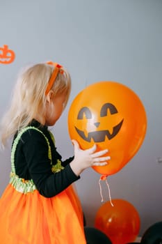 Children's Halloween - a girl in a witch hat and a carnival costume with airy orange and black balloons at home. Ready to celebrate Halloween.