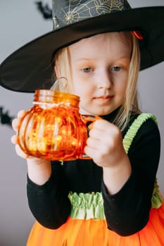 Children's Halloween - a girl in a witch hat and a carnival costume with airy orange and black balloons at home. Ready to celebrate Halloween.