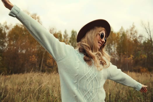 Autumn portrait of stylish modern happy young woman having fun and dancing, fashionable girl smiling in hat, sweater outdoors in park, warm fall season