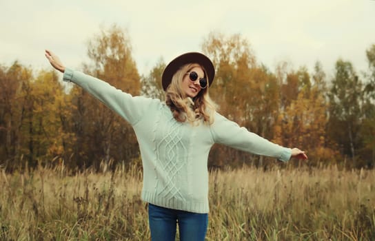 Autumn portrait of stylish modern happy young woman having fun and dancing, fashionable girl smiling in hat, sweater outdoors in park, warm fall season