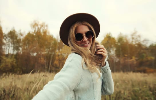 Autumn portrait of stylish modern happy young woman having fun and dancing, fashionable girl smiling in hat, sweater outdoors in park, warm fall season