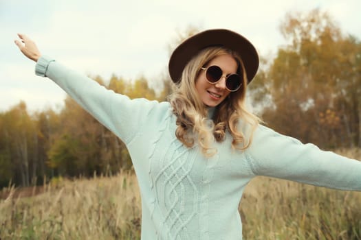 Autumn portrait of stylish modern happy young woman having fun and dancing, fashionable girl smiling in hat, sweater outdoors in park, warm fall season