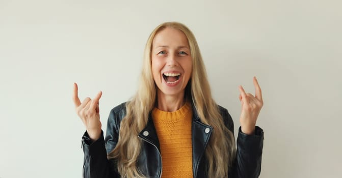 Portrait of happy stylish emotional mature woman overjoyed with crazy expression doing rock symbol with hands up, fashionable middle aged female having fun on white studio background