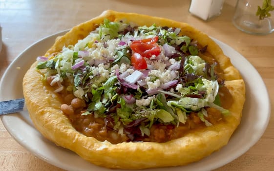 Close-up shot of a Navajo Taco, a traditional Native American frybread topped with beans, lettuce, tomatoes, cheese, and onions, served in an Arizona restaurant. Fresh and tasty ingredients - USA