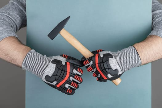 Man's arm in protective gloves of construction worker or building contractor holding hammer on blue paper background