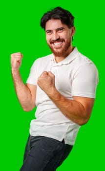 Happy man celebrating success with raised fists, wearing a white shirt against a bright green background close up