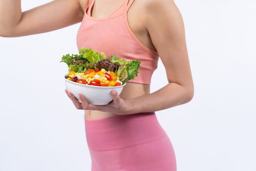 Young sporty Asian woman in sportswear holding salad bowl fill with vibrant of fruit and vegetable. Natural youthful and fit body lifestyle with balance nutrition on isolated background. Vigorous