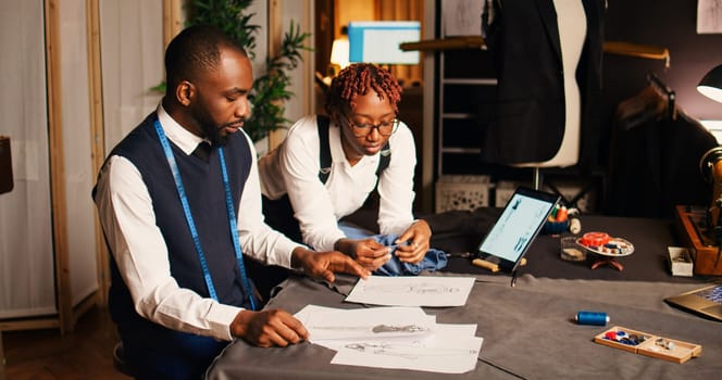 African american tailors picking fabric to create luxury fashion collection with tailoring tools and equipment. Man and woman designers working with materials, handcraft process.