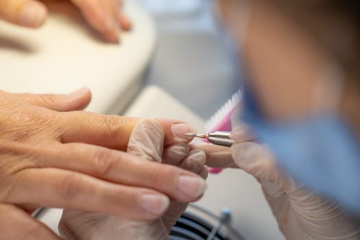 Nail care procedure in a beauty salon. Female hands and tools for manicure, process of performing manicure in beauty salon. Gloved hands of a skilled manicurist cutting cuticles. Concept spa body care