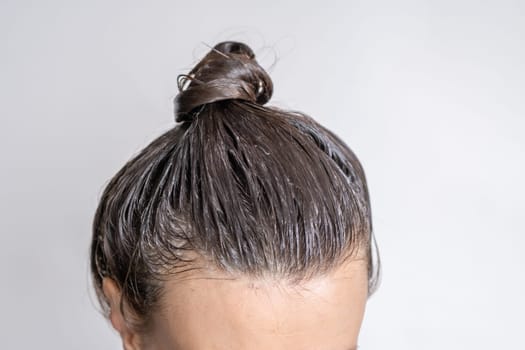 Close-up of a woman's heClose-up of a woman's head in the process of hair coloring on a white background. Closeup woman hands dyeing hair using a brush. Colouring of white hair at home.