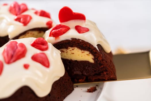 Slicing freshly baked red velvet bundt cake with chocolate lips and hearts over cream cheese glaze for Valentine's Day.