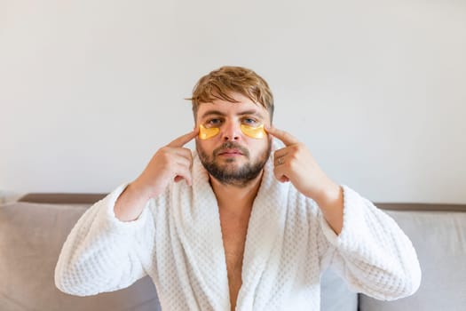 Beauty treatments, skin care, metrosexual concept. A handsome bearded man with golden bandages under his eyes makes funny faces with facial expressions.