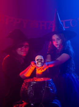 Two halloween witches making a potion and conjure with skull in halloween night. Magic, holidays and mystic concept.