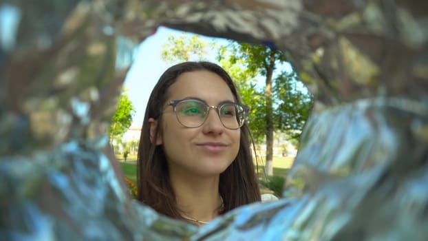 A young woman with glasses eats potato chips from a pack while walking in the park. View of a woman from a bag of chips. 4k