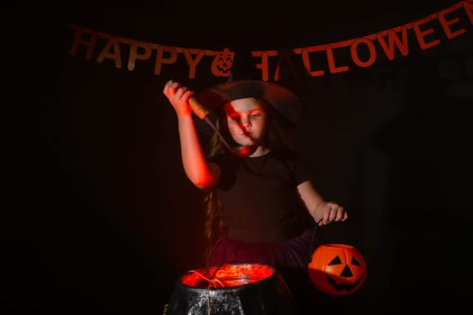 Child girl witch preparing a potion in the cauldron at halloween holidays