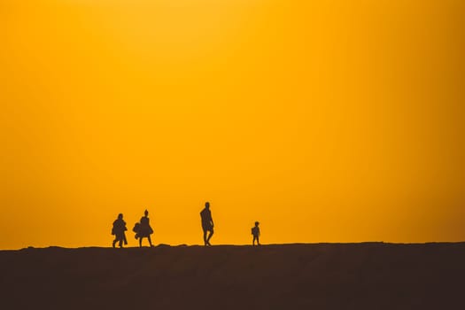 Silhouettes of people walking on a hill at a bright sunset. Mid shot