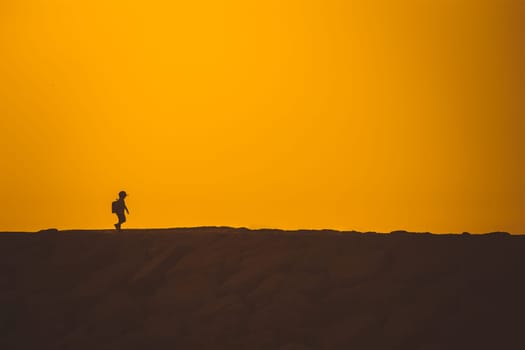 Silhouette of a little boy standing on the hill at sunset. Mid shot
