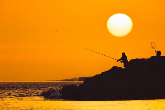 Black silhouette of a man fishing at sunset. Mid shot