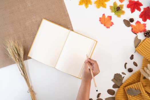 desk and the young woman who was taking notes with yellow-red autumn leaves on white background with copy space. work table with office supplies. concept cosy, cozy, seasonal autumn.