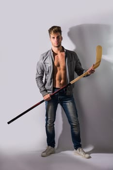 A shirtless man holding a hockey stick and a hockey puck