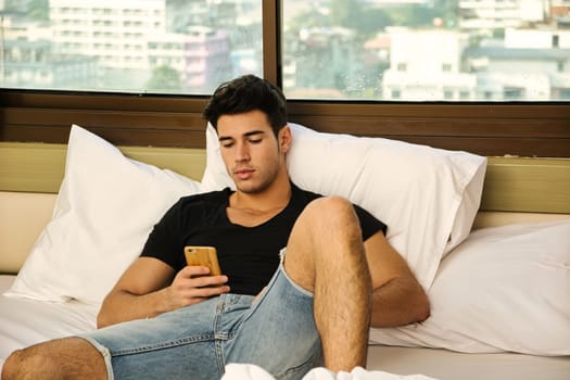 A man sitting on a bed looking at his cell phone