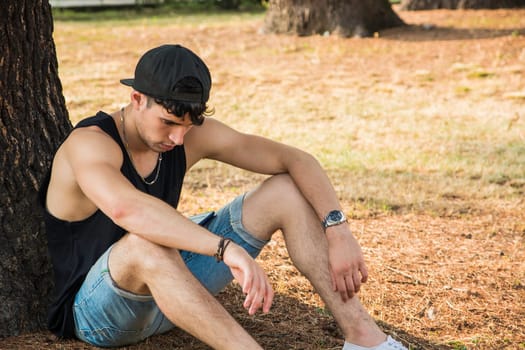 A man sitting against a tree in a park, tired, sad or depressed, thinking with his head down