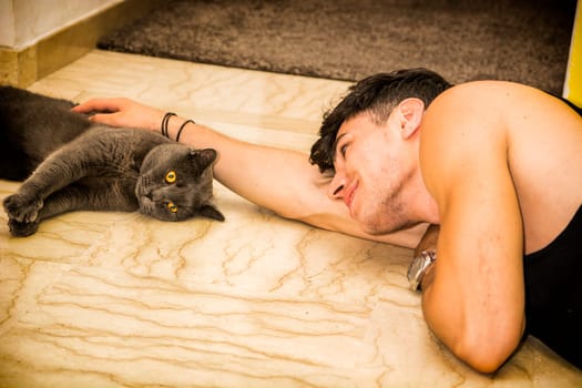 A man laying on the floor with a cat. Photo of a young, attractive man lying on the floor with a cat