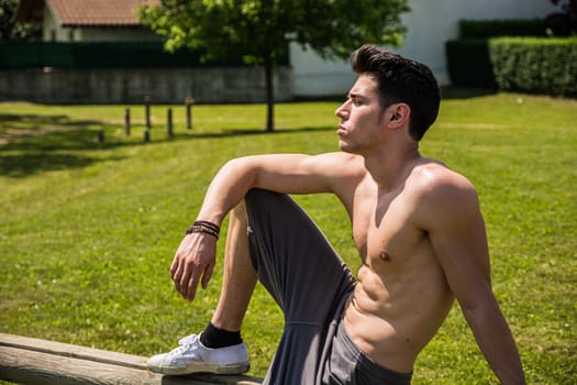 A shirtless man sitting on a bench in a park. Photo of a man enjoying a peaceful moment on a park bench