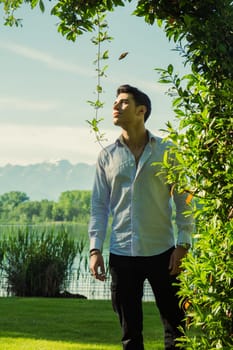 A man standing under a tree in a park. Photo of a man standing under a beautiful tree in a peaceful park