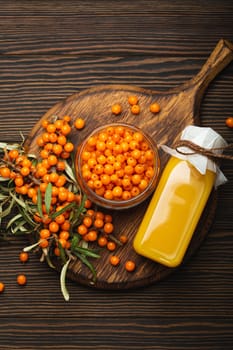 Sea buckthorn healthy drink in bottle, ripe berries in glass jar and branches with leaves top view on dark wooden rustic background, great for skin, heart, vessels and immune system..