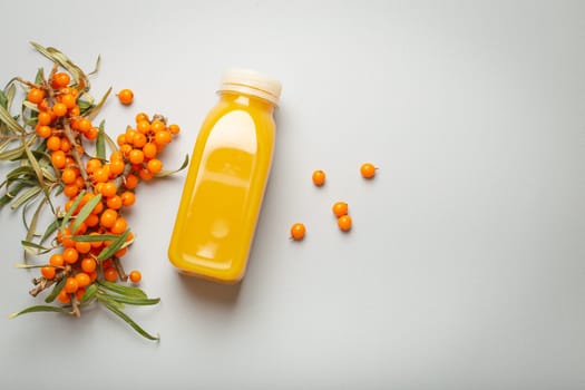 Sea buckthorn healthy juicy drink in bottle and branches with leaves and ripe berries top view on light grey simple background. Space for text..