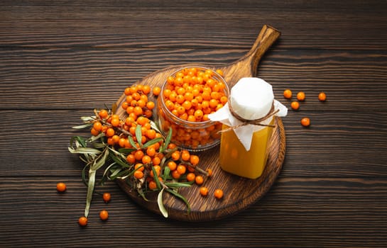 Sea buckthorn healthy drink in bottle, ripe berries in glass jar and branches with leaves top view on dark wooden rustic background, great for skin, heart, vessels and immune system..