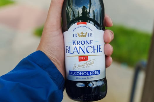 Tyumen, Russia-August 10, 2024: hand grasps a chilled bottle of alcohol-free Krone Blanche while sitting on a swing in a sunny park